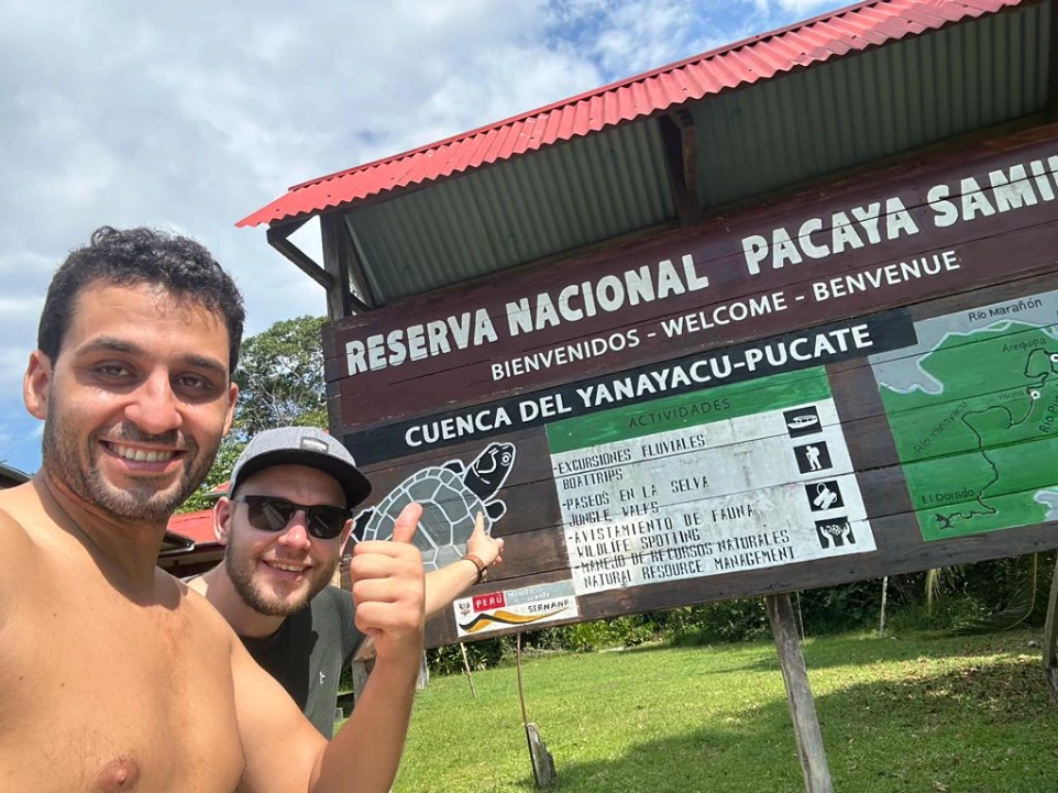 Dos exploradores sonrientes frente al letrero oficial de la Reserva Nacional Pacaya Samiria en la cuenca del Yanayacu-Pucate durante un tour de Ceiba Jungle Expeditions.