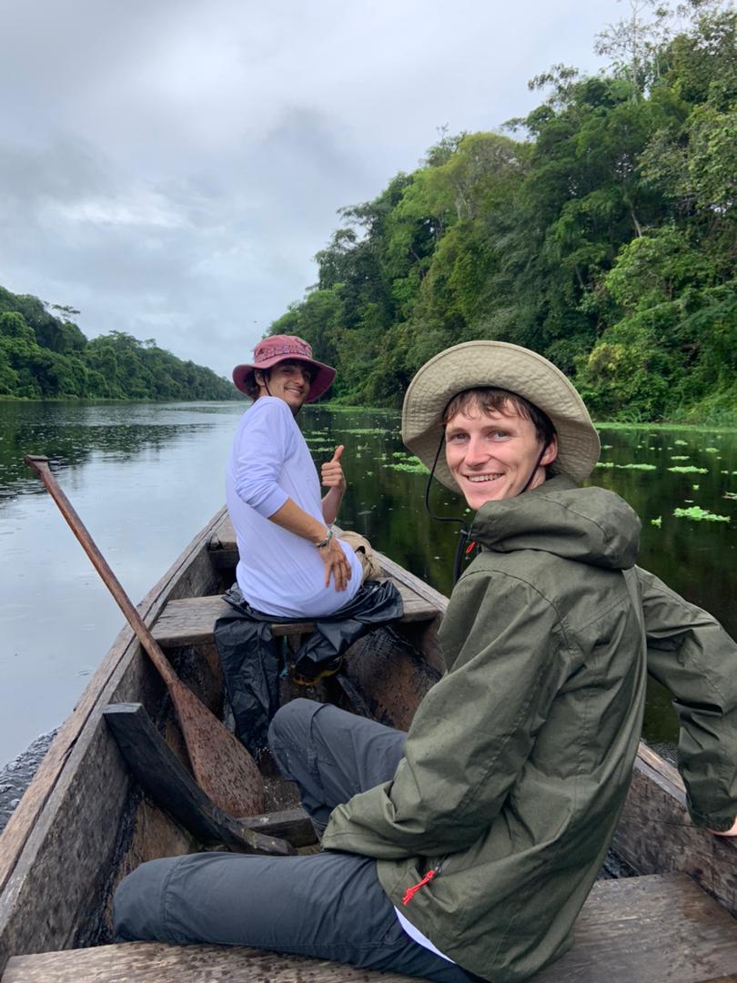 Dos observadores de aves equipados con ropa técnica de selva navegando en una canoa tradicional por un afluente tranquilo, en busca de especies raras durante una expedición de Ceiba Jungle Expeditions.